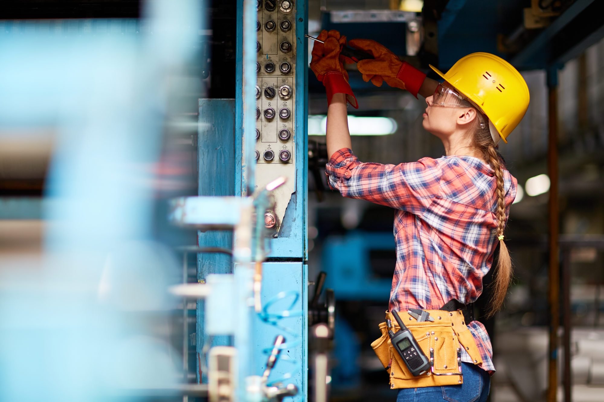 Female electrician or technician with screwdriver repairing machine at plant