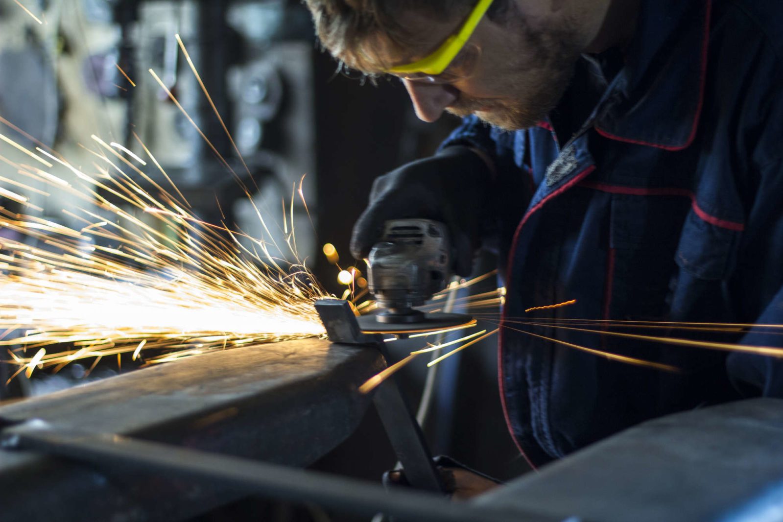 Factory worker using electric grinder in metal industry.