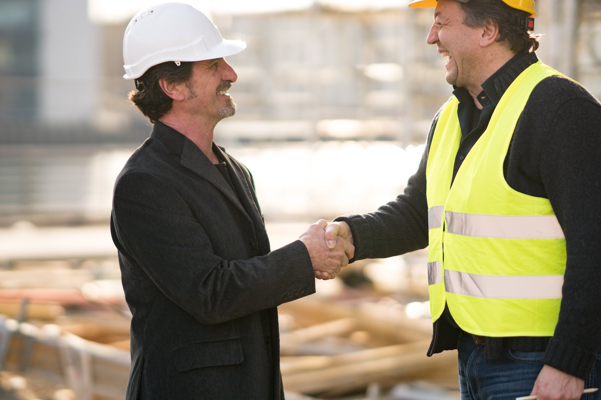 men shaking hands on job site wearing hard hats
