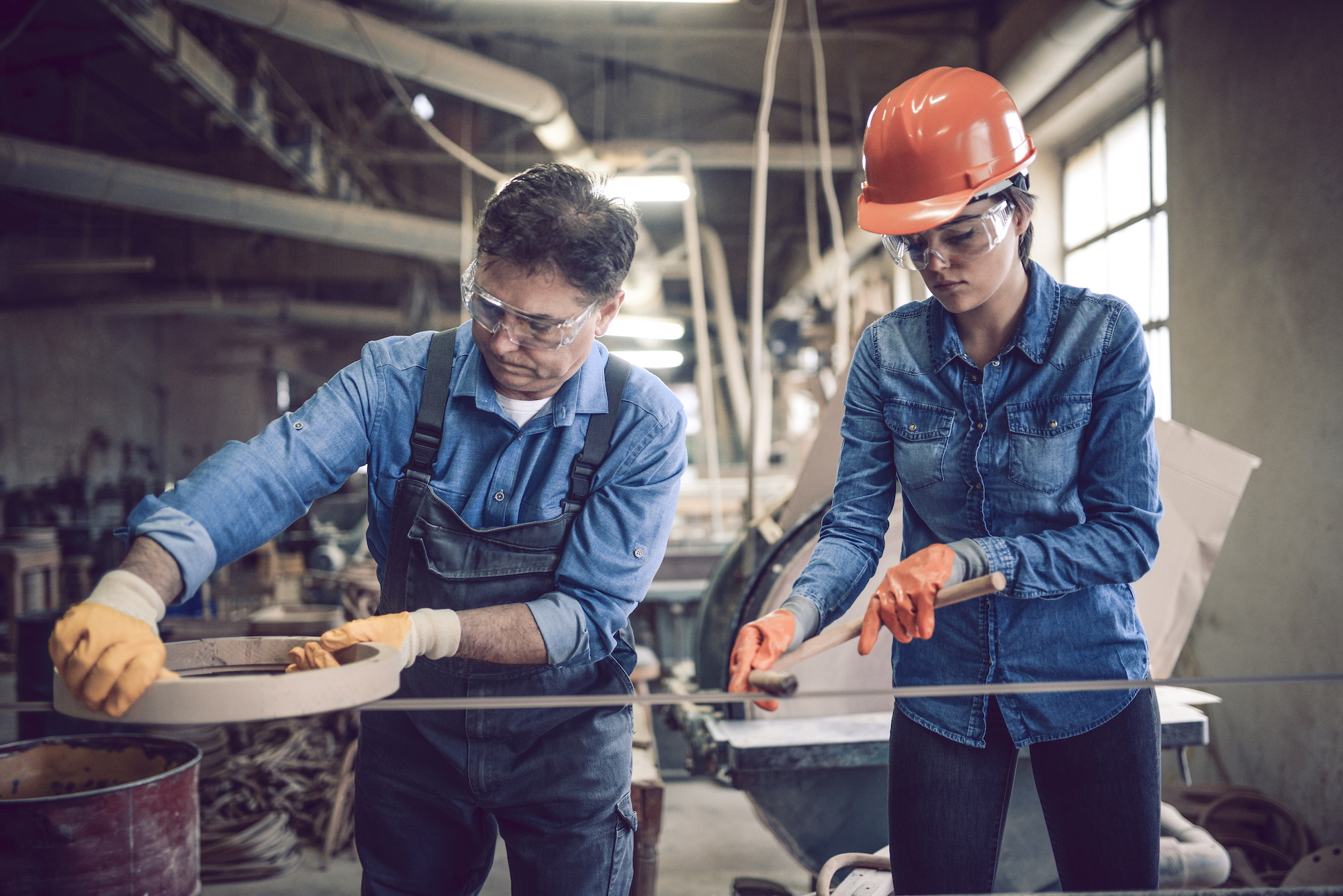 tradesman and tradeswoman working in shop with protective glasses