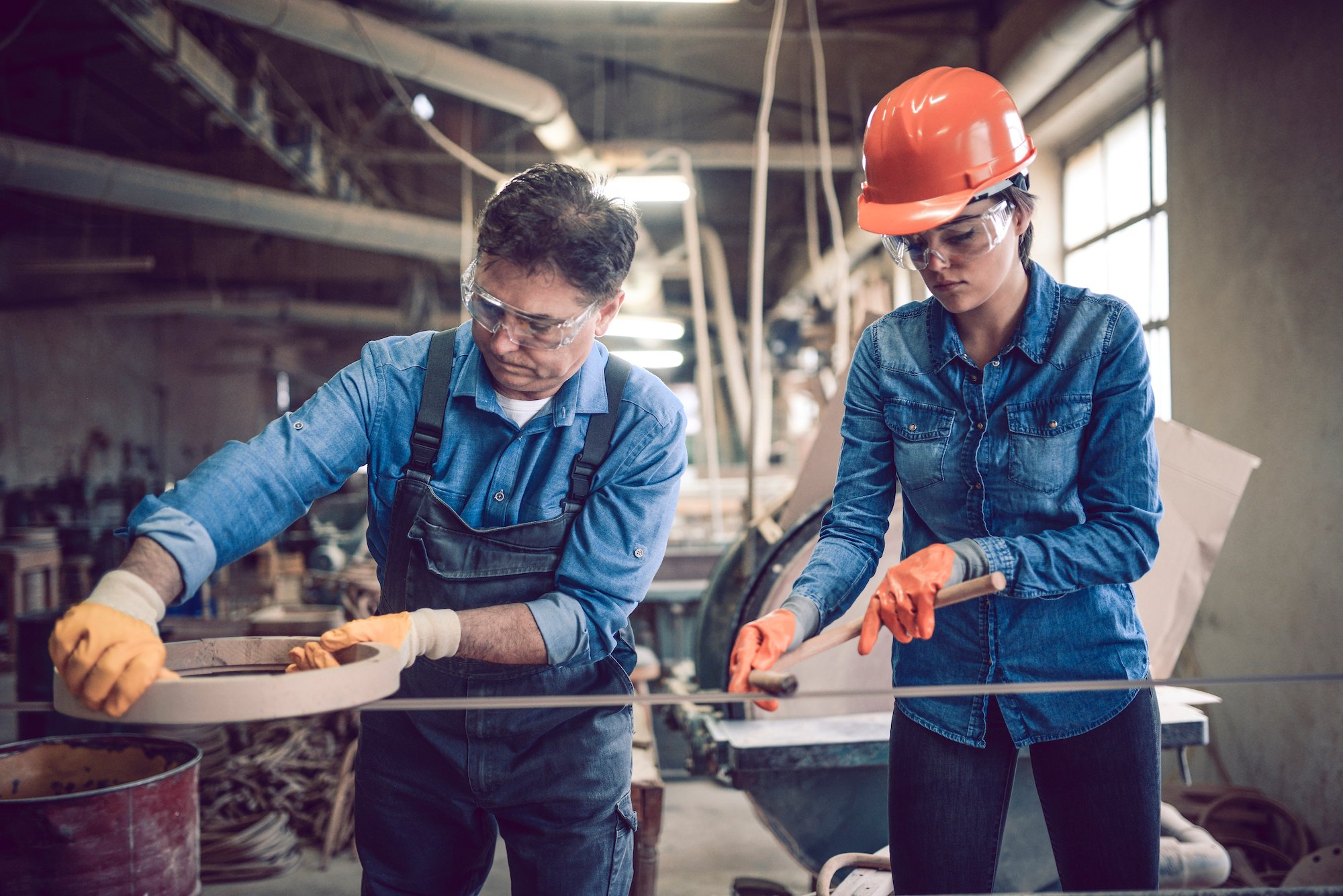 tradesman and tradeswoman working in shop with protective glasses